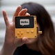 A person holds up a small, yellow electronic device with the word "Hello" on its screen.